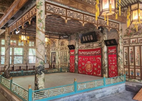 The columns of the theater stage are intricately carved and decorated with beautiful patterns, with two vintage Chinese lanterns beside them.