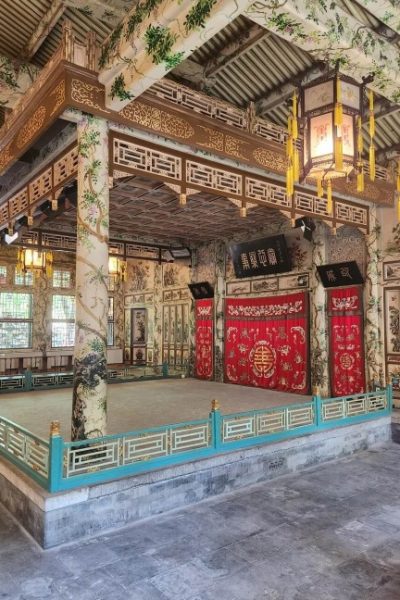 The columns of the theater stage are intricately carved and decorated with beautiful patterns, with two vintage Chinese lanterns beside them.