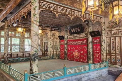 The columns of the theater stage are intricately carved and decorated with beautiful patterns, with two vintage Chinese lanterns beside them.