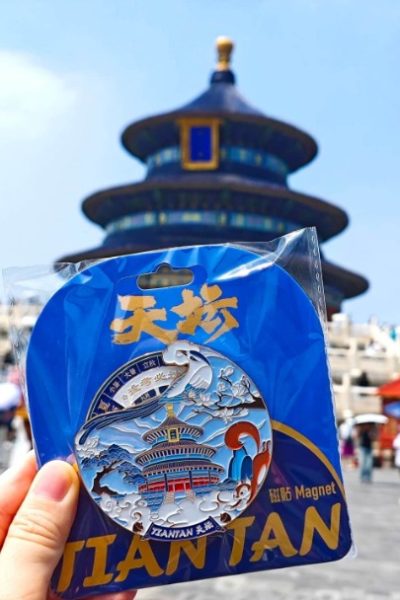 Tourists are holding up their fridge magnets shaped like the Hall of Prayer for Good Harvests for a photo.