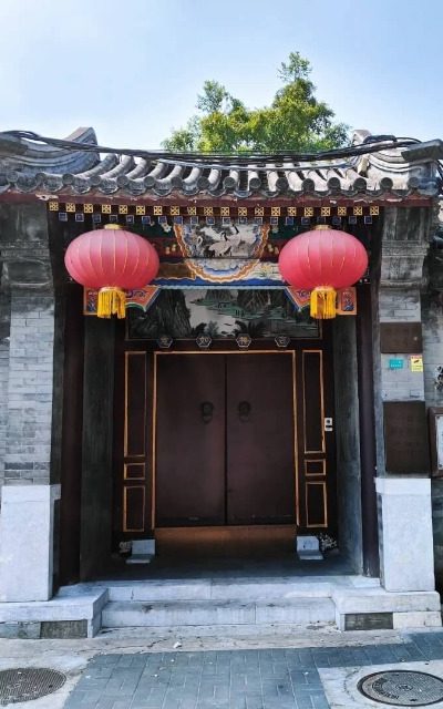 The courtyard entrance in a Beijing hutong features two traditional red lanterns hanging from the door.