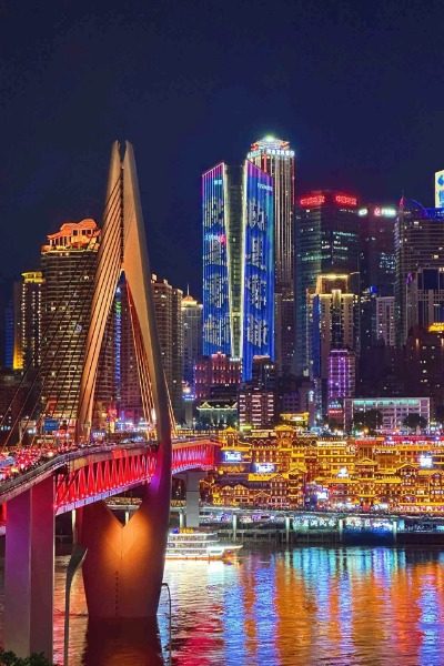 The Qiansimen Bridge in Chongqing lights up with red lights, while the nearby Hongya Cave glows with golden yellow lights.