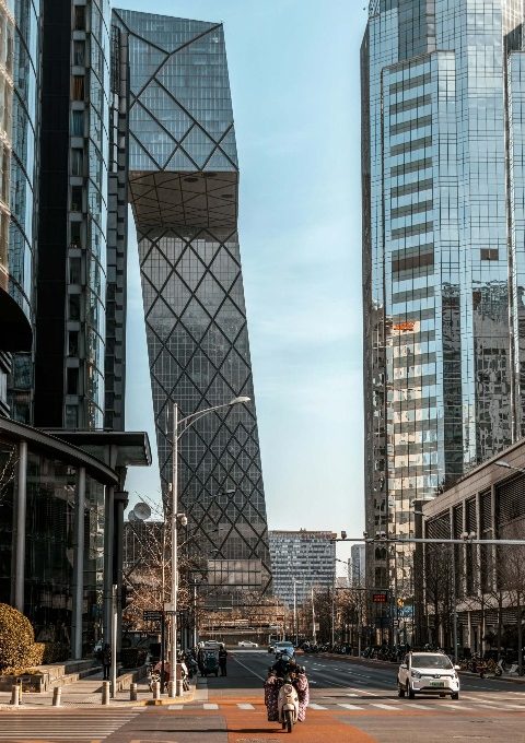 Cars and motorcycles are driving on the road, with the iconic CCTV Headquarters building in the background.