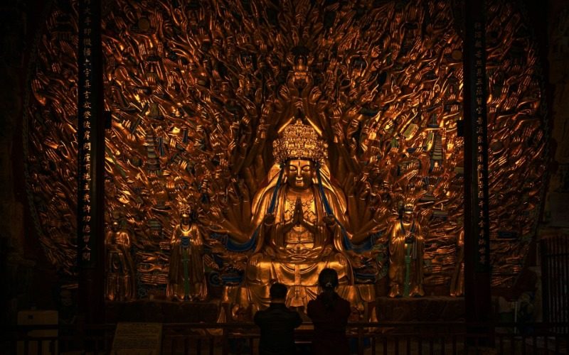 At the Dazu Rock Carvings, tourists are kneeling and praying in front of the Thousand-Hand Guanyin.