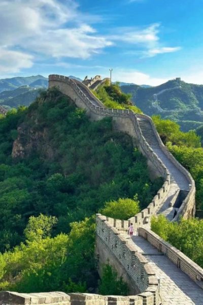 The blue sky and lush green trees highlight the grandeur of the Badaling Great Wall.